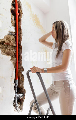 Donna che guarda la danno dopo un tubo di acqua di perdita a casa Foto Stock