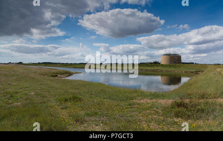 Un Martello Tower in piedi dietro un piccolo lago e riflessa in esso con le nuvole e il cielo blu, Suffolk, Inghilterra Foto Stock