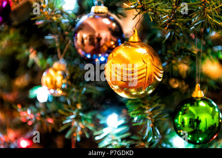 Primo piano di appendere illuminato in arancione, verde, blu, colorato, multicolore, multi-colore di ornamento di Natale su albero di pino con luci Foto Stock