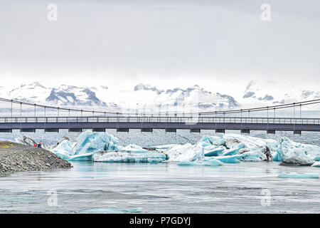 Jokulsarlon laguna glaciale, lago glaciale in Islanda con molti iceberg galleggianti, rotta uno 1 ponte su acqua con persone, Vatnajokull montagne, cli Foto Stock