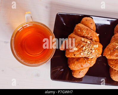 La colazione è eccellente e salutare con burro e cereali e croissant su tray nero e sbiancato tavolo in legno con una tazza di acqua calda, aromatici e profumati tè Foto Stock