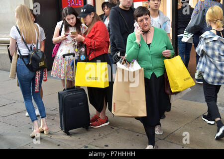 Gli amanti dello shopping e ai turisti il trasporto delle borse della spesa a piedi passato il grande magazzino Selfridges di Oxford Street nel centro di Londra. Foto Stock