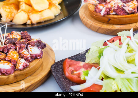 Insalata e piatto in legno di stile galiziano polpo cucinato con patate, paprica e olio d'oliva. Pulpo a la gallega Foto Stock