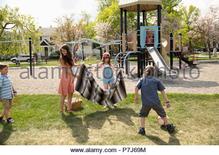 Madre e bambini che giocano, diffondendo Coperta picnic nel parco di sole