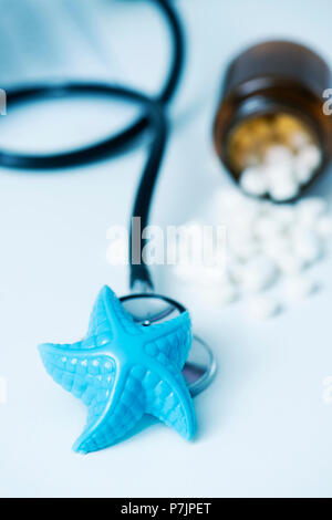 Primo piano di una plastica blu starfish e alcune pillole su un banco medici, in un ufficio di medici, raffigurante l'assistenza medica in estate Foto Stock