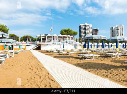 Vista del Bagno numero 6' bar sulla spiaggia con lettini e ombrelloni e alta sorge in background, architettura sulla spiaggia di Lignano Foto Stock
