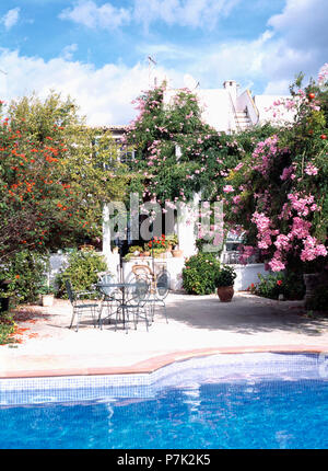 Le rose rosa e sedie in metallo e tavolo sulla terrazza accanto alla piscina di fronte della piccola casa di Maiorca Foto Stock