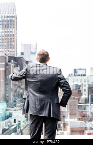 Retro del giovane imprenditore in piedi in stropicciata business suit guardando New York City cityscape skyline di Manhattan dopo intervista a rompere Foto Stock