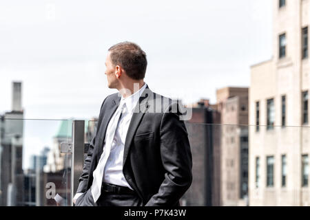 Giovane imprenditore in piedi in business suit guardando sopra la spalla a New York City cityscape skyline di Manhattan dopo la pausa intervista a sky Foto Stock