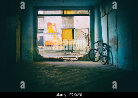 Una bicicletta è parcheggiata vicino a un grande buco su una parete di un edificio occupato dalla sede sociale il movimento con graffiti dipinti sulle pareti fatiscenti nel backg Foto Stock