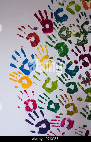 L'immagine verticale di rosso, blu, giallo, verde e viola handprints su un bianco muro di cemento. Foto Stock