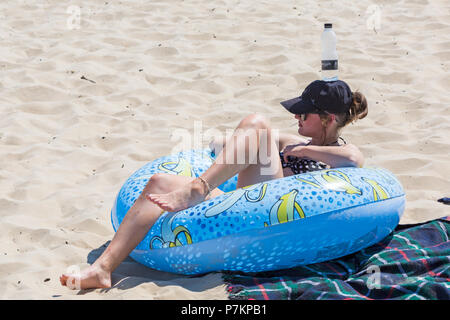 Bournemouth, Dorset, Regno Unito. 7th luglio 2018. Tempo nel Regno Unito: Un'altra calda giornata di sole mentre l'ondata di caldo continua e migliaia di amanti del sole si dirigano verso il mare con temperature che aumentano per godersi le spiagge sabbiose di Bournemouth sulla costa meridionale anche con la grande partita! Tenere una bottiglia d'acqua a portata di mano! Giovane donna rilassante prendere il sole in ciambella gonfiabile anello con una bottiglia d'acqua sulla testa. Credit: Carolyn Jenkins/Alamy Live News Credit: Carolyn Jenkins/Alamy Live News Credit: Carolyn Jenkins/Alamy Live News Foto Stock