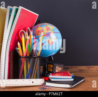 Assortimento di accessori per la scuola su di un desktop con un vuoto di sfondo blackboard Foto Stock