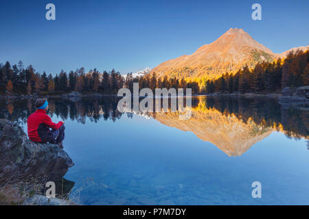 Escursionista prendere una pausa per ammirare il tramonto sul lago di Saoseo e il mais da Murasciola mount, Poschiavo, val di Campo del Cantone dei Grigioni, Svizzera, Europa Foto Stock