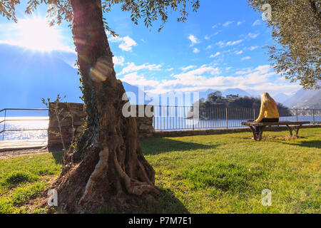 Una ragazza ditting su un banco di fronte all'Isola Comacina, Ossuccio, Lago di Como, Lombardia, Italia, Europa. Foto Stock