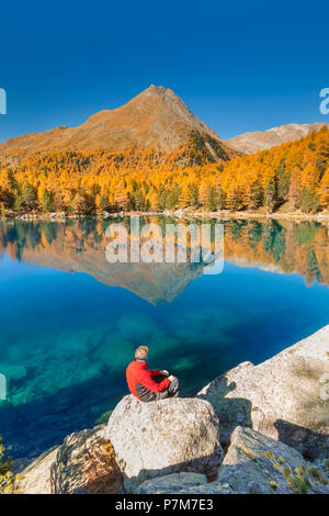 Escursionista prendere una pausa per ammirare il lago Saoseo in una perfetta giornata autunnale, Poschiavo, val di Campo del Cantone dei Grigioni, Svizzera, Europa Foto Stock
