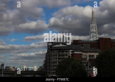 La vista dal ponte di millenaria lungo il Tamigi come la luce del sole colpisce il Tower Bridge e la Shard, lasciando il resto della zona in ombra profonda. Nuvoloso. Foto Stock