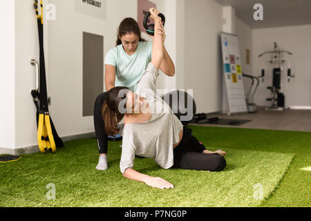 Fisioterapista assistendo giovane donna caucasica con esercizio con il manubrio durante la riabilitazione in palestra in ospedale. Fisioterapista femmina tr Foto Stock