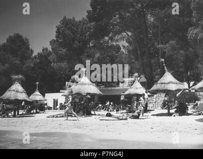 Islas Baleares. Mallorca. Playa de Formentor. Bañistas tumbados en la arena protegidos del sol con sombrillas de Paja. Años 1950. Foto Stock