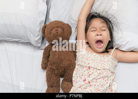 Bambina sbadiglio e dormire sul letto con Teddy bear bambola, assistenza sanitaria e concetto di rilassamento Foto Stock