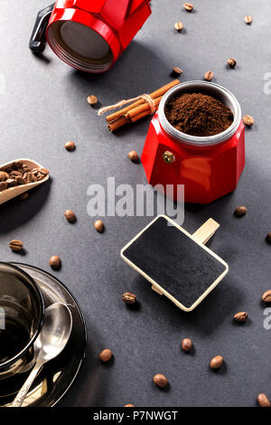 I chicchi di caffè fritti vicino alla macchina del caffè e la scheda di scrittura su sfondo nero tabella Foto Stock