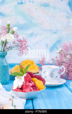 Gelato di diversi colori su sfondo blu. Il lampone e mango. Il decor di fiori e il caffè di mattina Foto Stock