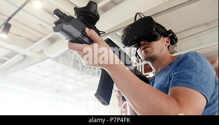 Ragazzo giocando VR gioco cecchino con la pistola e bicchieri Foto Stock