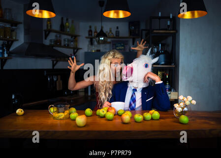 Coppia insolita trascorrere del tempo insieme al banco bar in appartamenti eleganti con cibo e bevande. Funny Girl scared strano ragazzo in maschera comico Foto Stock