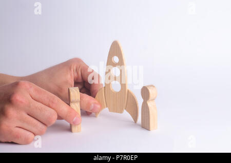 Un razzo in legno e figure di persone nelle mani degli uomini. Un uomo sta giocando con un razzo e figure umane. Il minimalismo, spazio di viaggio e turismo, com Foto Stock