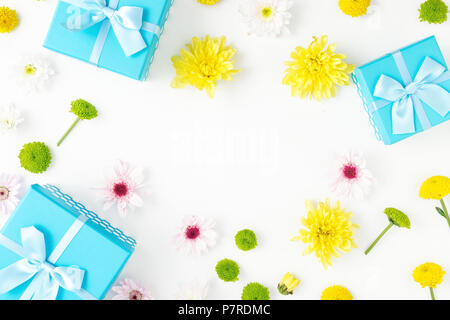 Telaio del blu scatole regalo raccolta e crisantemi su uno sfondo bianco nel piatto stile di laici. Vista superiore Foto Stock