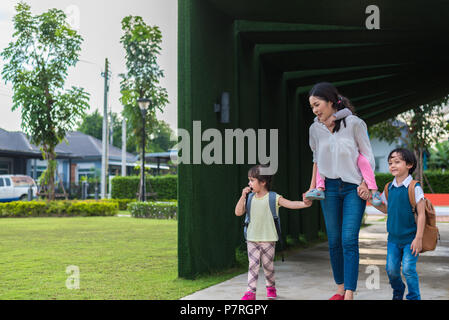 Mamma single che trasportano e giocare con i suoi figli in giardino con parete verde dello sfondo. Persone e stili di vita del concetto. La famiglia felice e Home sweet hom Foto Stock