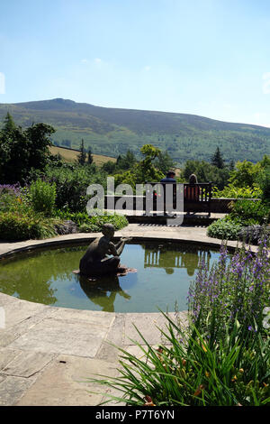 Un giovane seduto su una panca in legno guardando Simon di guida nella sala Parcevall giardini, Skyreholme, Appletreewick, Wharfedale, nello Yorkshire, Inghilterra, Regno Unito. Foto Stock