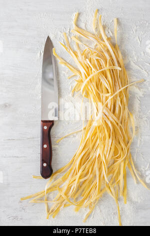 Materie tagliatelle fatte in casa con un grosso coltello da cucina su uno sfondo bianco, vista dall'alto Foto Stock