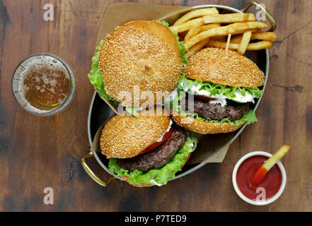 Hamburger con costolette di manzo e patatine fritte sono serviti in una padella sul tavolo di legno con birra e ketchup, vista dall'alto Foto Stock