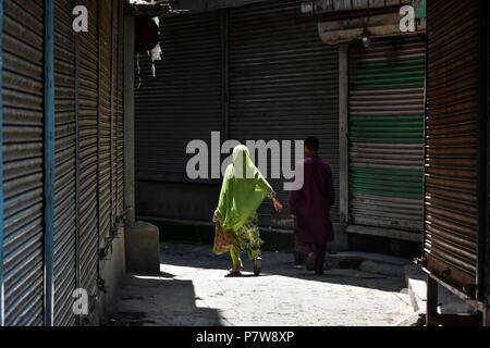 Srinagar, India. 8 Luglio, 2018. I locali del Kashmir a piedi passato negozi chiusi durante il coprifuoco imposto alla vigilia del secondo anniversario della morte del comandante ribelle Burhan Muzaffar Wani in Srinagar. Burhan e i suoi collaboratori sono stati uccisi in questo giorno nel 2016 innescando una massiccia anti-india rivolta nel Kashmir. Durante la rivolta di più di 90 persone sono state uccise, circa 15.000 feriti tra di essi 950 ricevuto lesioni agli occhi con pistole di pellet. Credito: Saqib Majeed SOPA/images/ZUMA filo/Alamy Live News Foto Stock