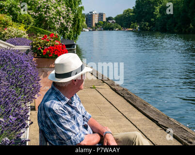 Il fiume Tamigi, Hampton Wick, London, England, Regno Unito, 8 luglio 2018. Regno Unito: meteo persone divertirsi sul Tamigi su una Domenica mattina nel caldo sole l ondata di caldo. Un vecchio uomo che indossa un cappello di Panama si siede in una panchina dalla riva del sole Foto Stock