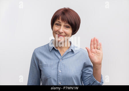 Positivo caucasici maturi donna sorridente cordiale e agitando la mano alla telecamera. Foto Stock
