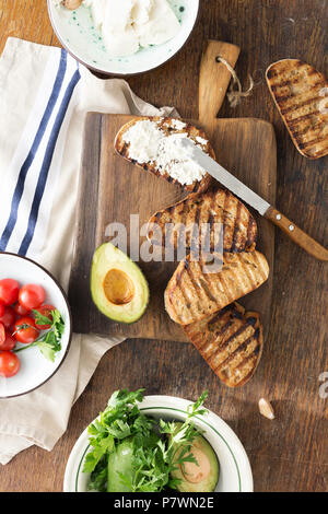 Top Visualizza set di ingredienti per la cottura di bruschette con formaggio feta, pomodorini e avocado su un tavolo di legno. Il cibo italiano Foto Stock