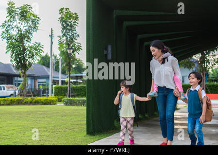 Mamma single che trasportano e giocare con i suoi figli in giardino con parete verde dello sfondo. Persone e stili di vita del concetto. La famiglia felice e Home sweet hom Foto Stock