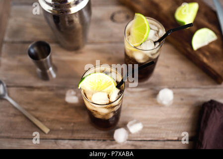 Il rum e la cola Cuba Libre drink con calce e ghiaccio su tavola in legno rustico Foto Stock