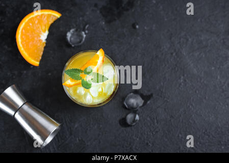 Il gin e il succo di arancia cocktail su sfondo nero, vista dall'alto. Estivo rinfrescante cocktail con vodka, ghiaccio, arancio e menta. Foto Stock