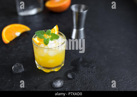 Il gin e il succo di arancia cocktail su sfondo nero, vista dall'alto. Estivo rinfrescante cocktail con vodka, ghiaccio, arancio e menta. Foto Stock