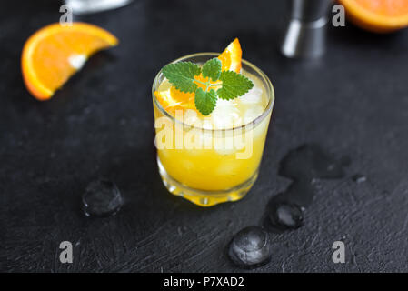 Il gin e il succo di arancia cocktail su sfondo nero, vista dall'alto. Estivo rinfrescante cocktail con vodka, ghiaccio, arancio e menta. Foto Stock