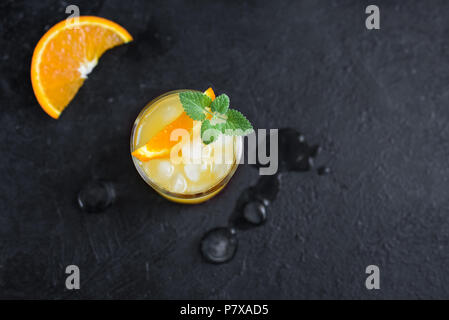 Il gin e il succo di arancia cocktail su sfondo nero, vista dall'alto. Estivo rinfrescante cocktail con vodka, ghiaccio, arancio e menta. Foto Stock