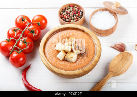 Zuppa Gazpacho con cracker, in un piatto di legno su un bianco sullo sfondo di legno. Nelle vicinanze si trovano i pomodori e spezie Foto Stock