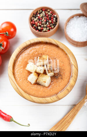 Zuppa Gazpacho con cracker, in un piatto di legno su un bianco sullo sfondo di legno. Nelle vicinanze si trovano i pomodori e spezie Foto Stock