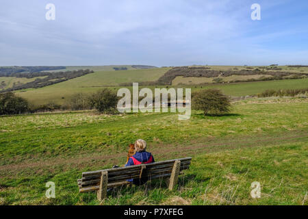 Vista posteriore di una signora contempating seduta su una panchina nel South Downs National Park. Ammirando il panorama. Foto Stock