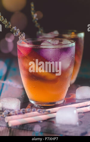 Peach aperol spritz con fette di pesche e l'acqua di lavanda sulla scrivania in legno. Foto Stock