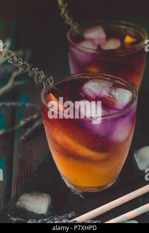 Peach aperol spritz con fette di pesche e l'acqua di lavanda sulla scrivania in legno. Foto Stock