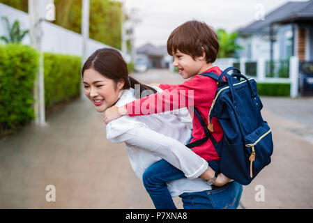 Mamma single che trasportano e giocare con i suoi figli vicino a casa con villa street sfondo. Persone e stili di vita del concetto. La famiglia felice e Home sweet h Foto Stock